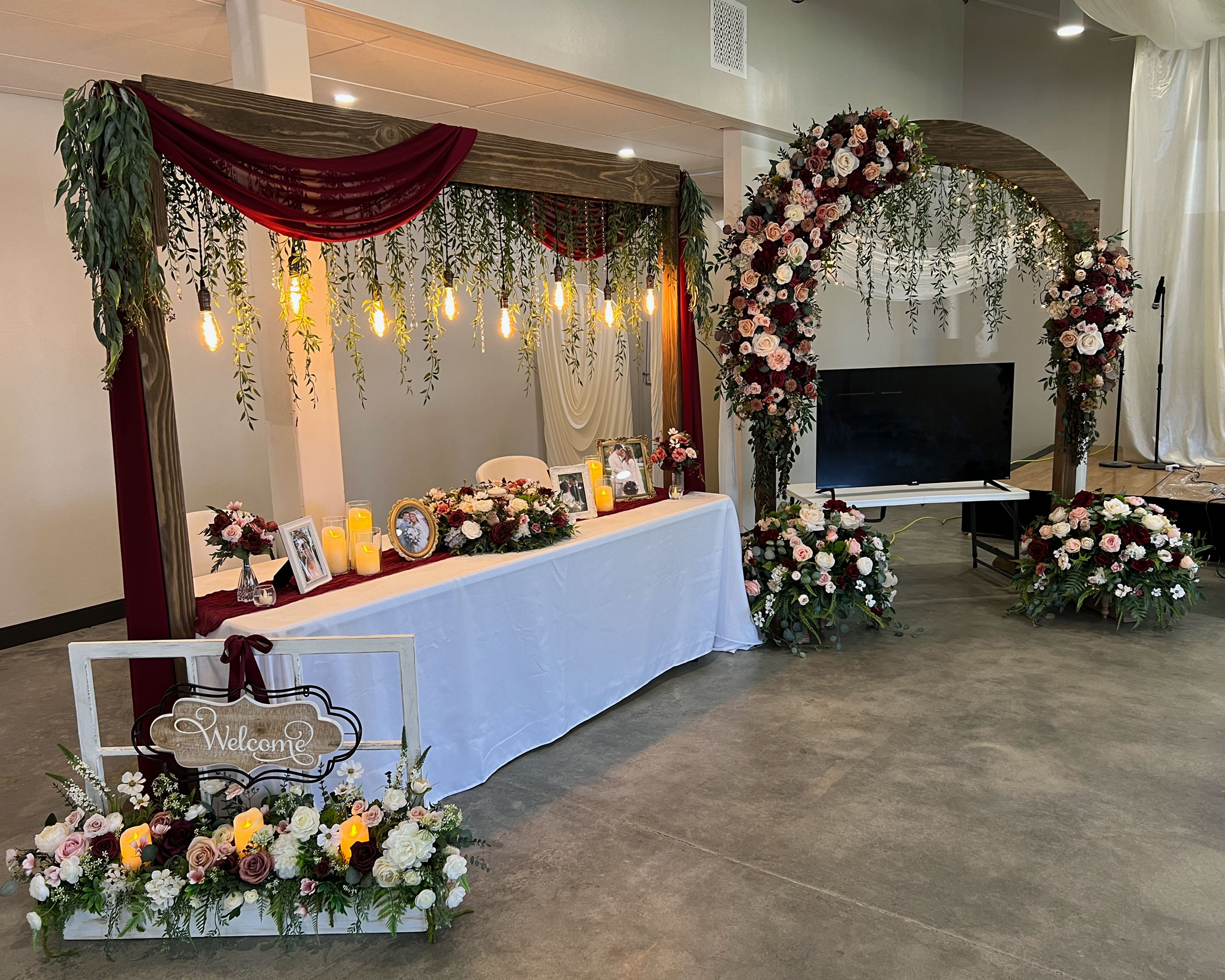 Event Booth featuring Burgundy Rose Ivory Floral on Rustic Weathered Wedding Arch and Lighted Table Arch at The Vale Venue in Provo, Utah
